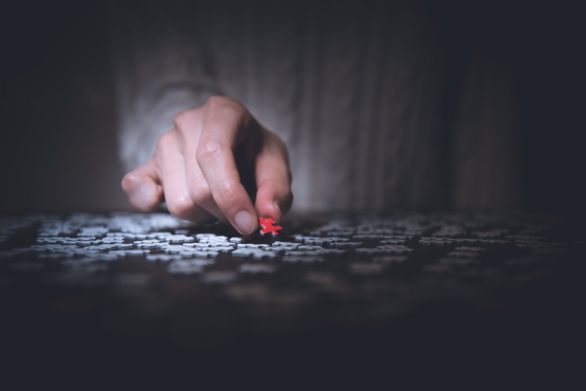 Hand picking a red puzzle piece out of grey ones