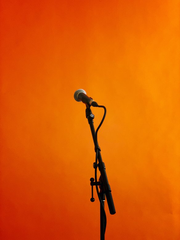 Black and grey microphone with stand in front of an orange background